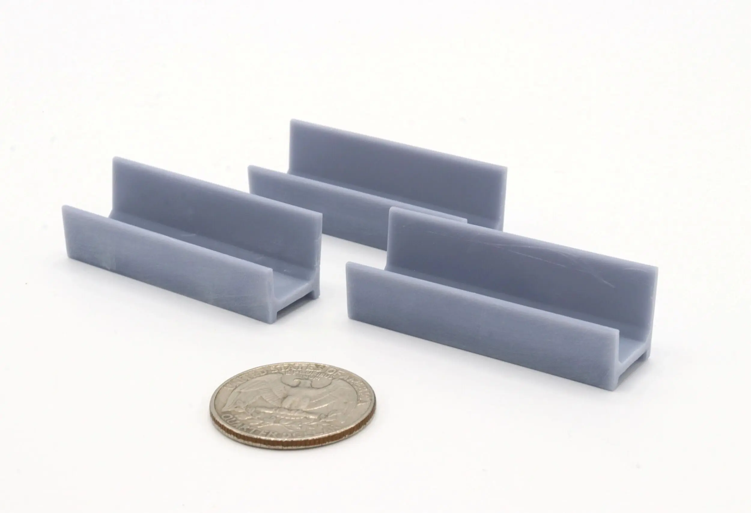 Four small gray plastic brackets with a coin for scale.