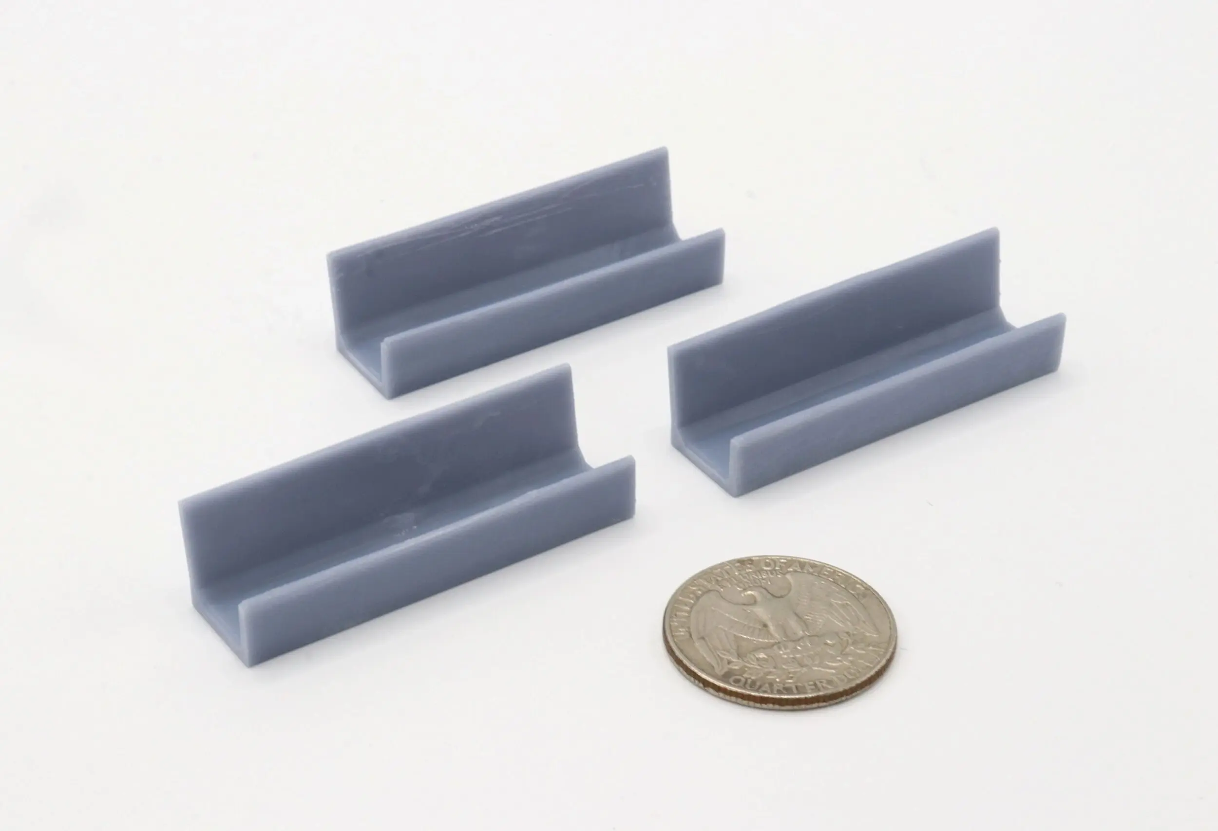 Four small gray plastic right-angle brackets next to a quarter for scale.