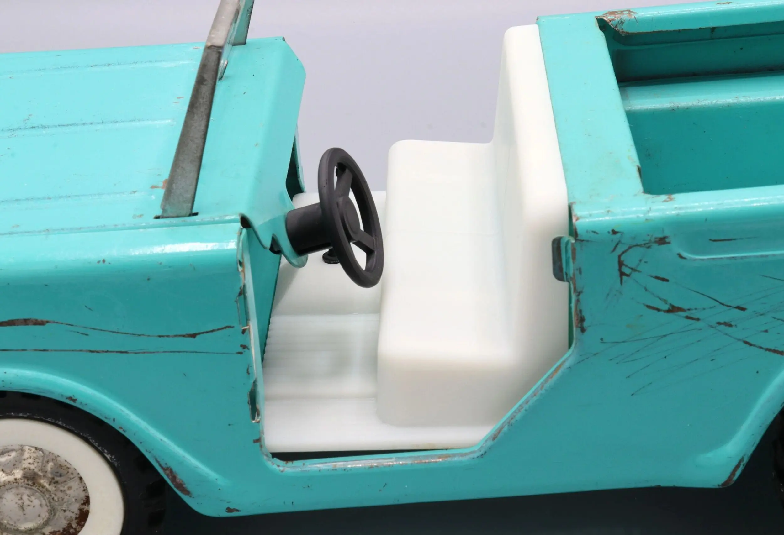 Close-up of a turquoise toy car's white interior and black steering wheel.