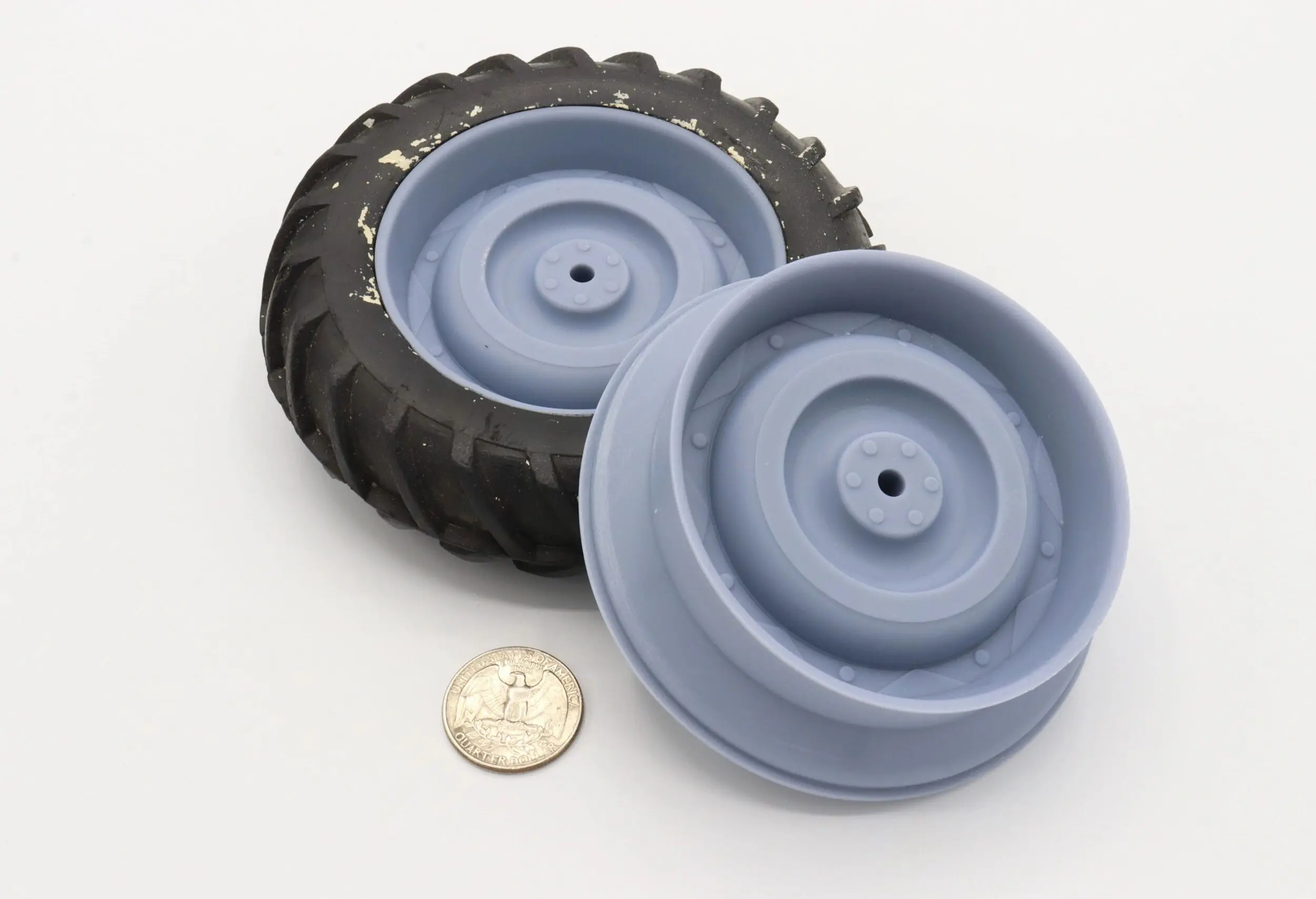 Two black and gray toy wheels with a coin for scale.