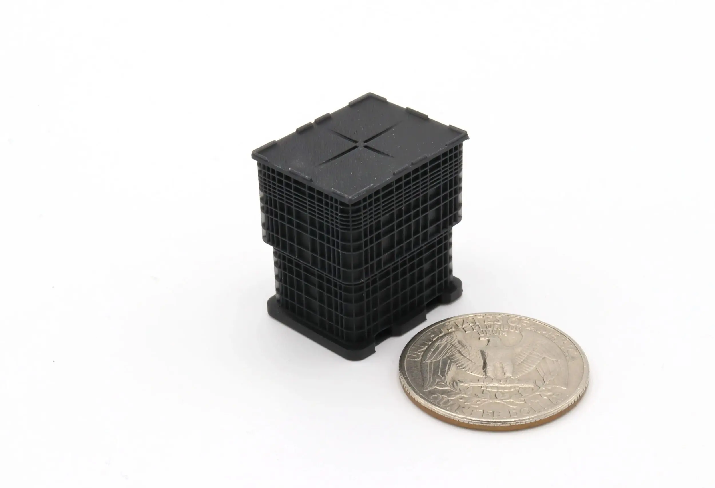 Small black plastic grid cube next to a quarter for scale.