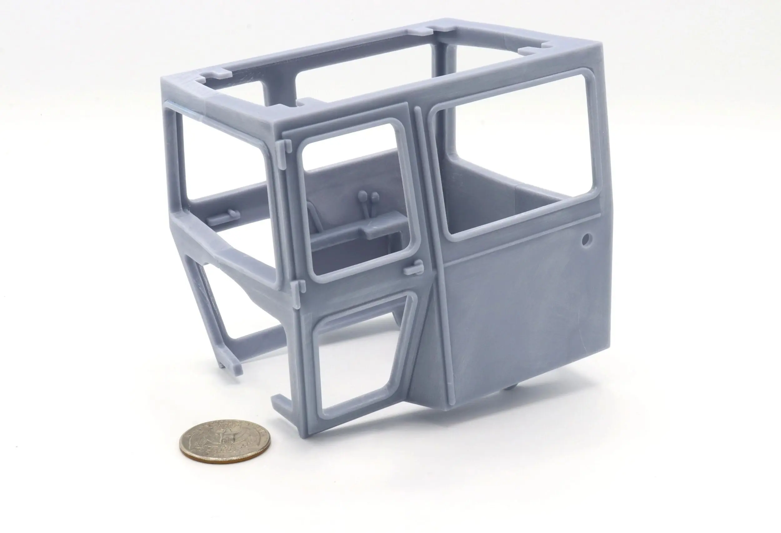 A miniature gray truck cab model next to a coin for scale.