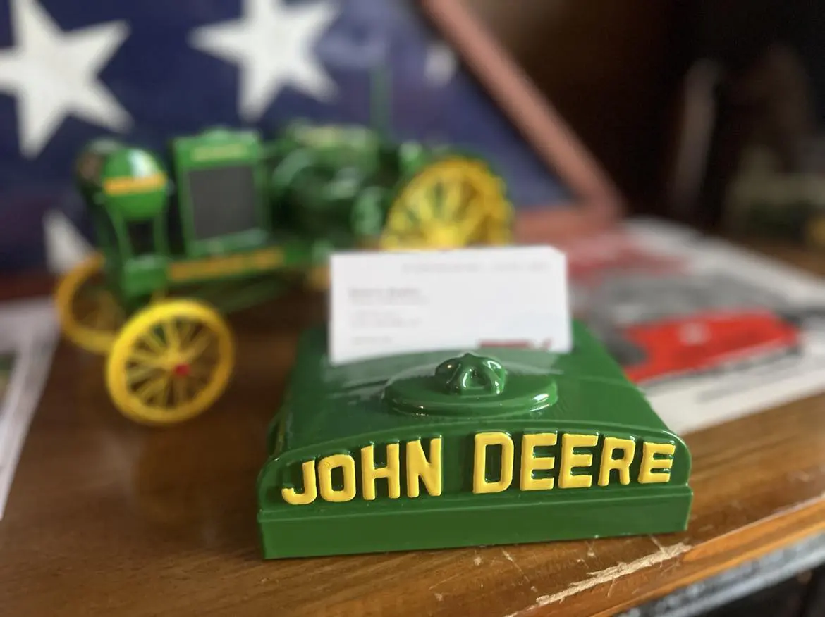 A miniature green John Deere tractor model with a business card holder.
