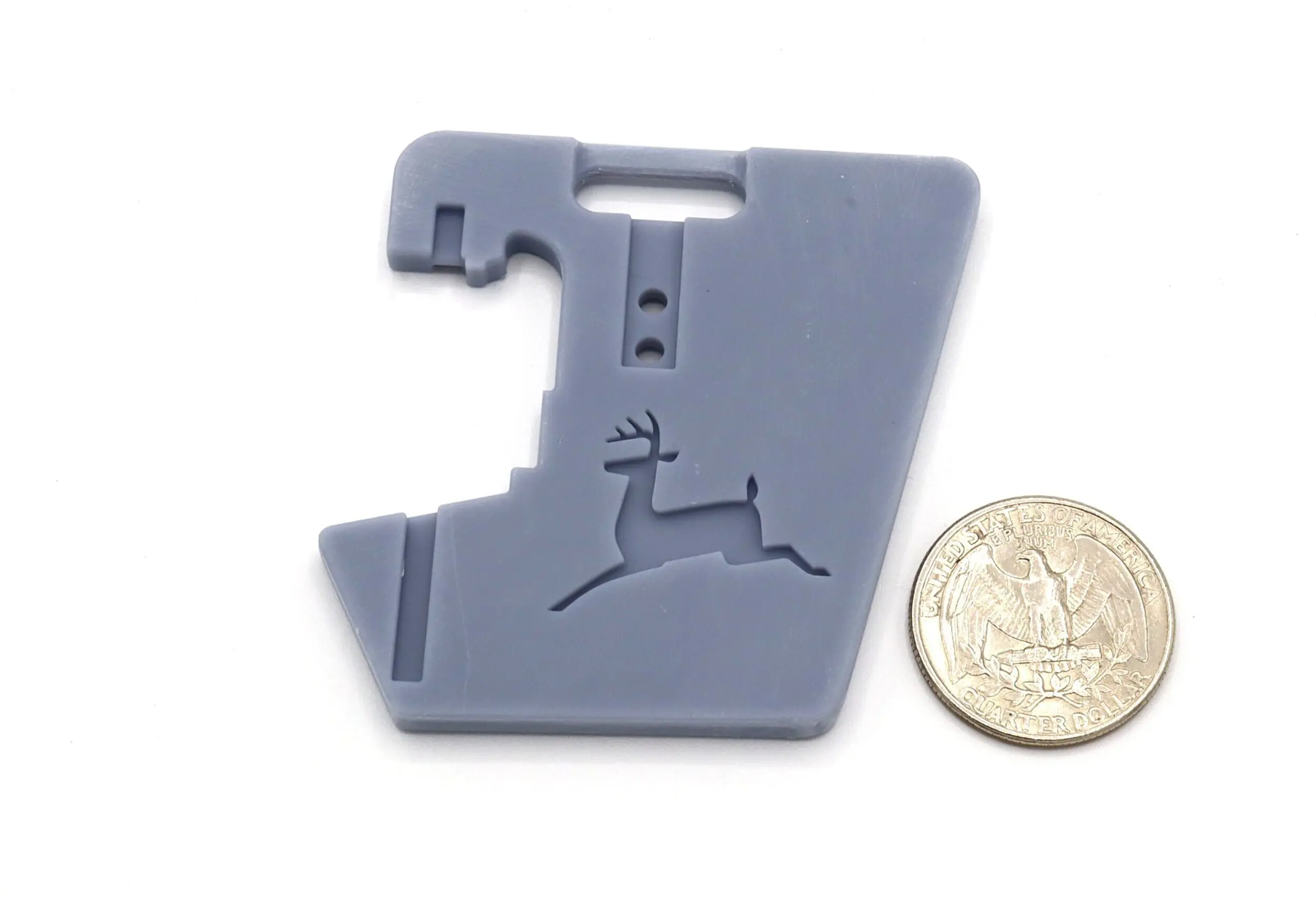 Gray tool with deer design beside coin.