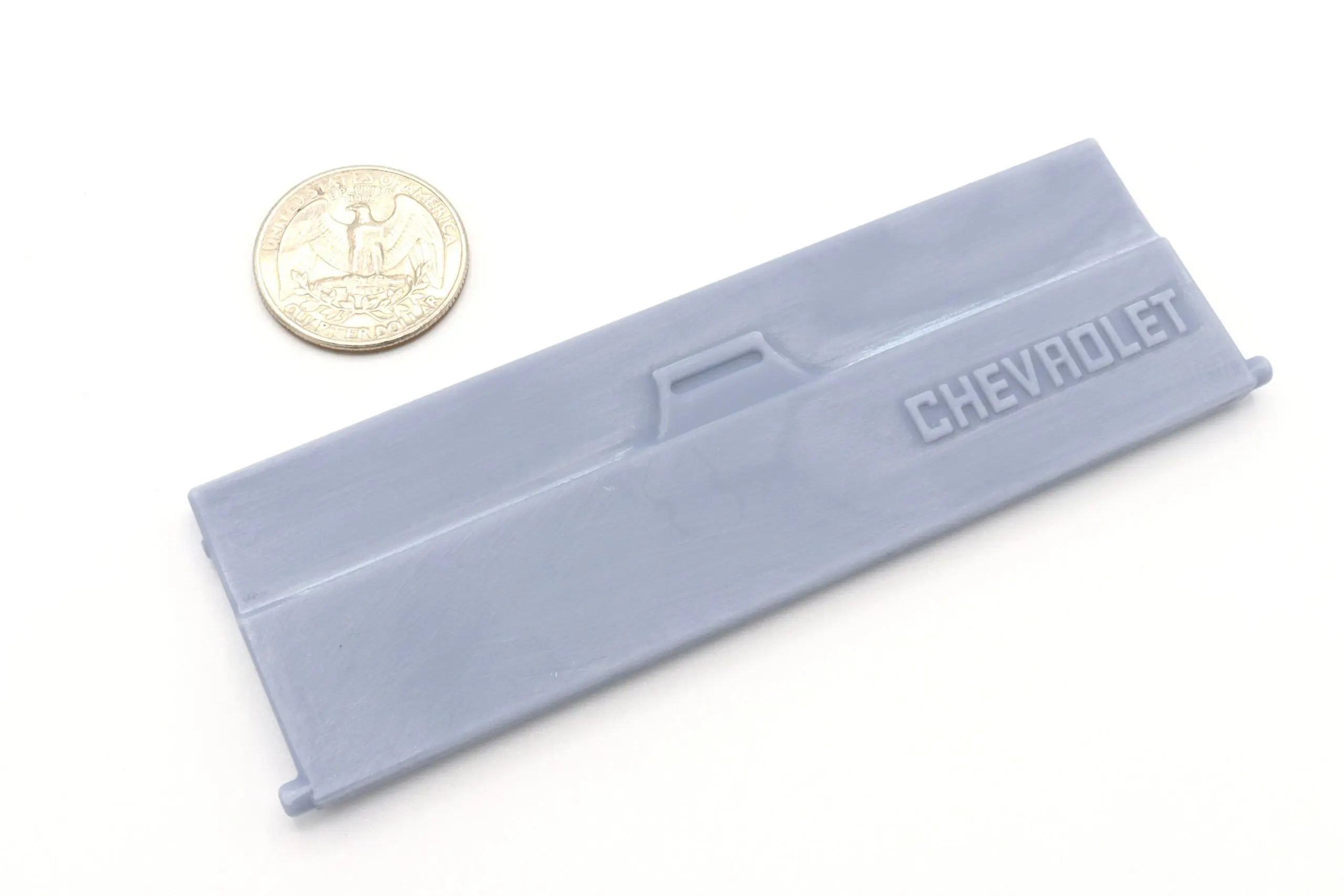 Plastic Chevrolet part with coin for scale.