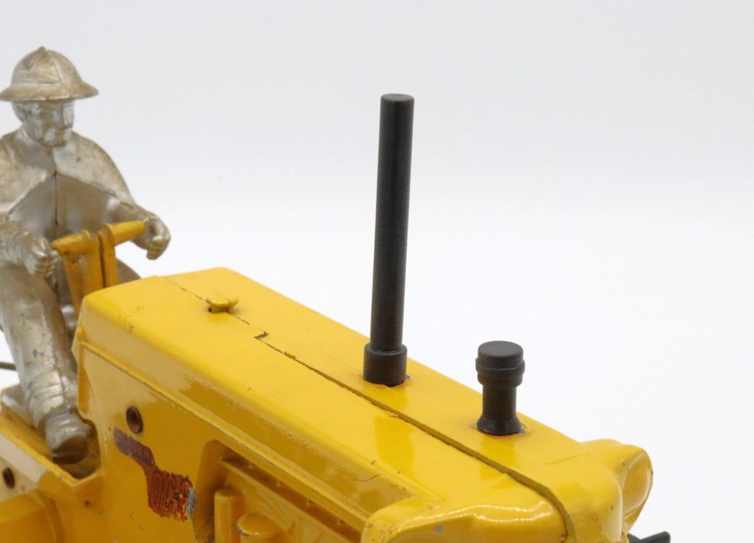 Close-up of a yellow model tractor with exhaust pipe and knob.