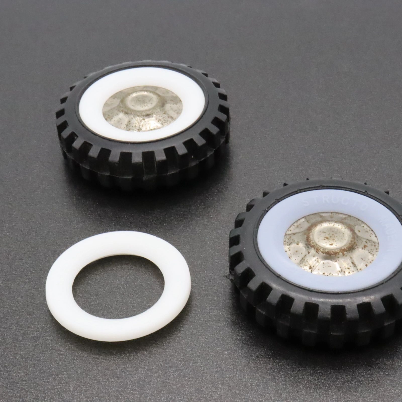 Two small mechanical gears with attached tires and a white washer on a gray surface.
