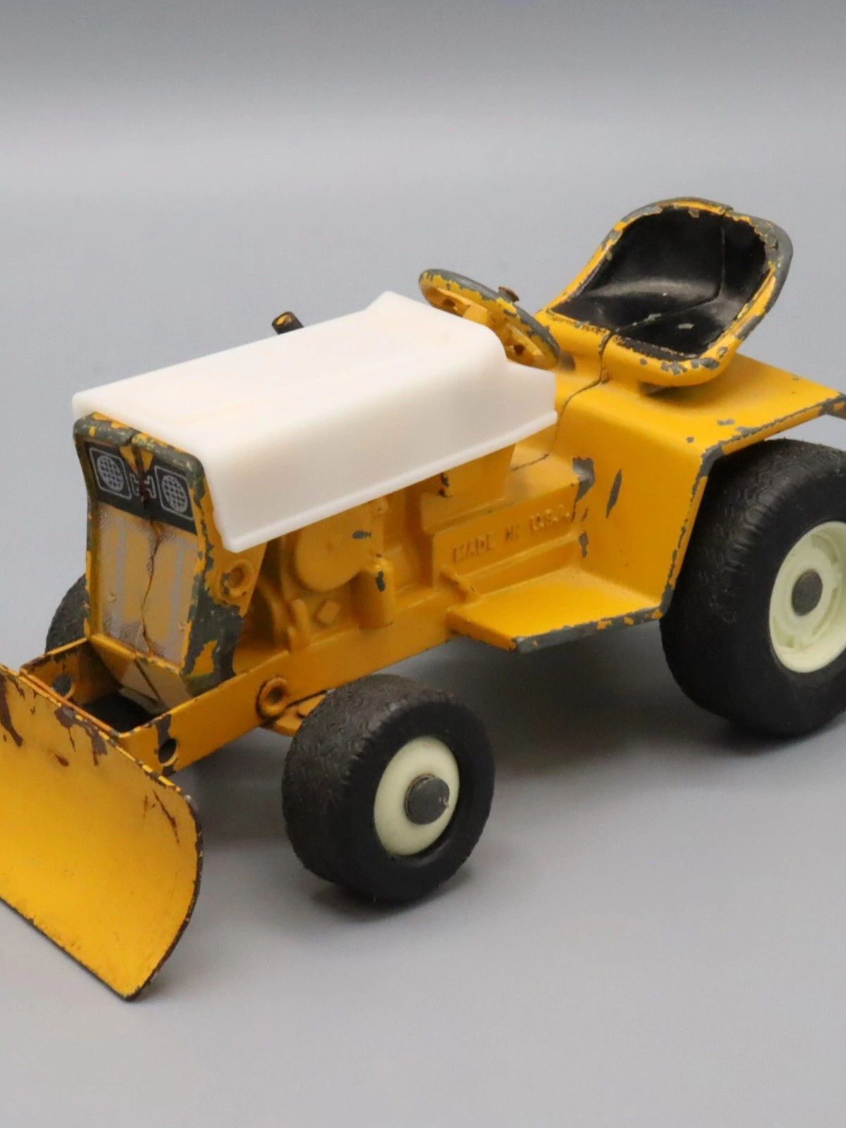 Yellow toy bulldozer with white roof and large rear wheels.