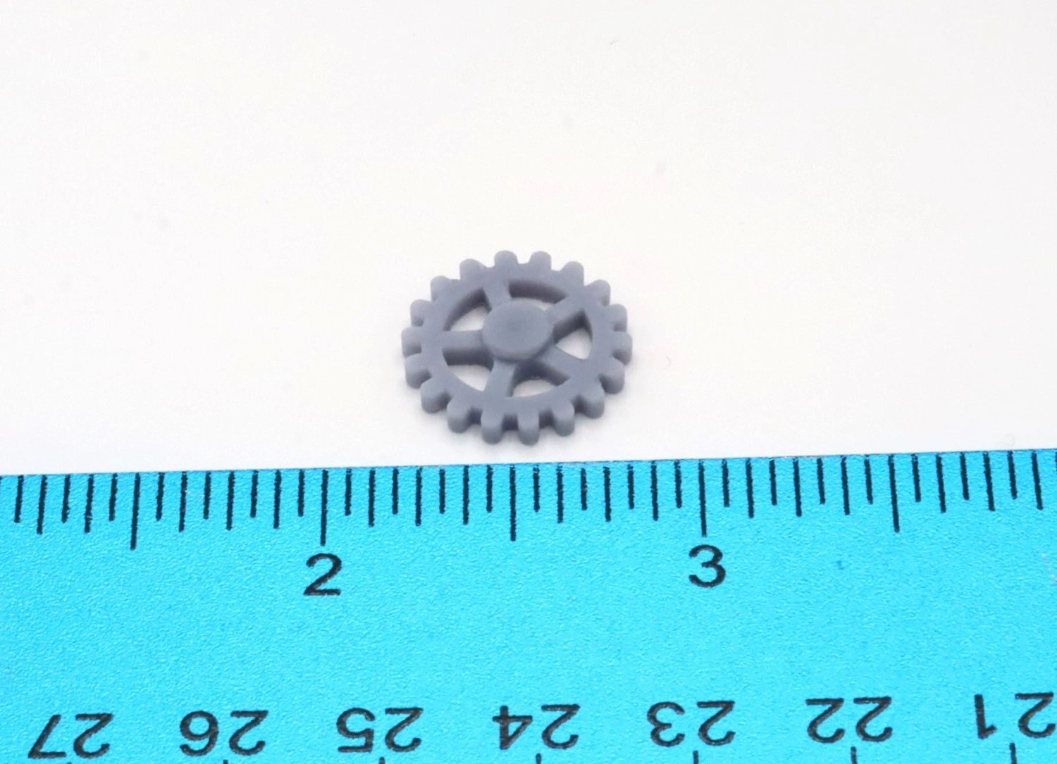A small gray plastic gear next to a blue ruler for scale.