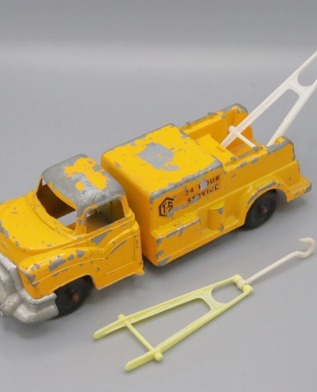 Vintage yellow tow truck toy with detachable hook and ladder.