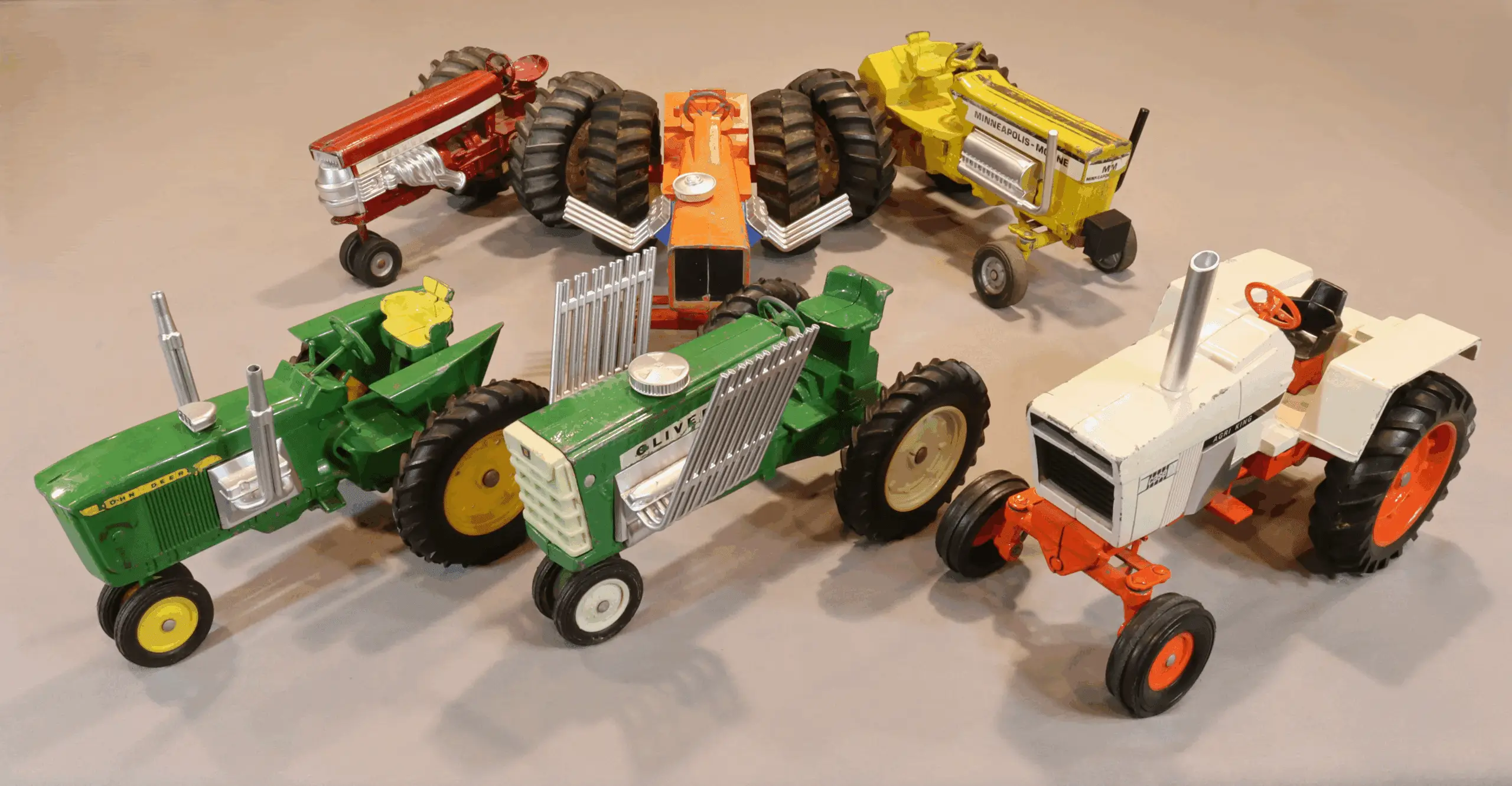 A collection of colorful toy tractors arranged on a beige surface.